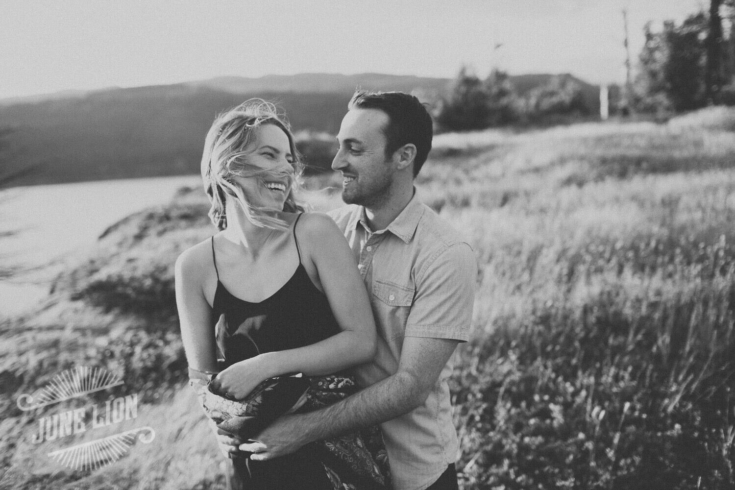 a couple laughing looking at each other standing on a grassy field (photograph by June Lion Photography)