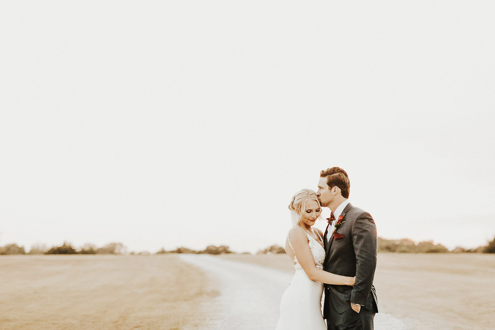 a wedding bride holding the groom while he kisses on her forehead