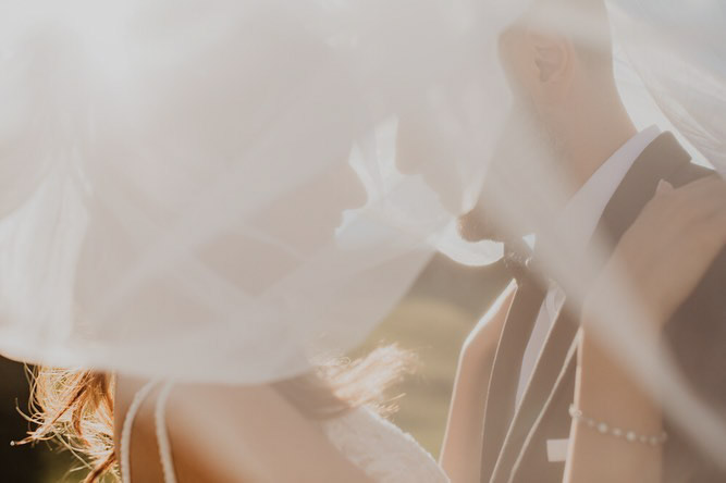 a bride and a groom embracing each other shrouded by the bridal veil