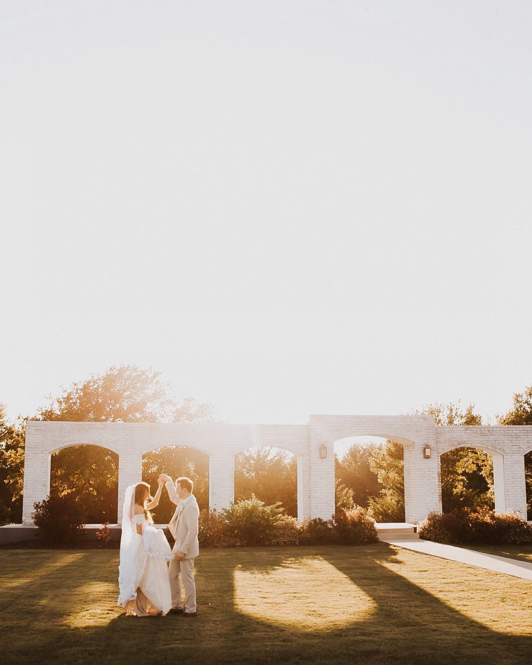 a couple dancing in their wedding attire in bright outdoor sunlight