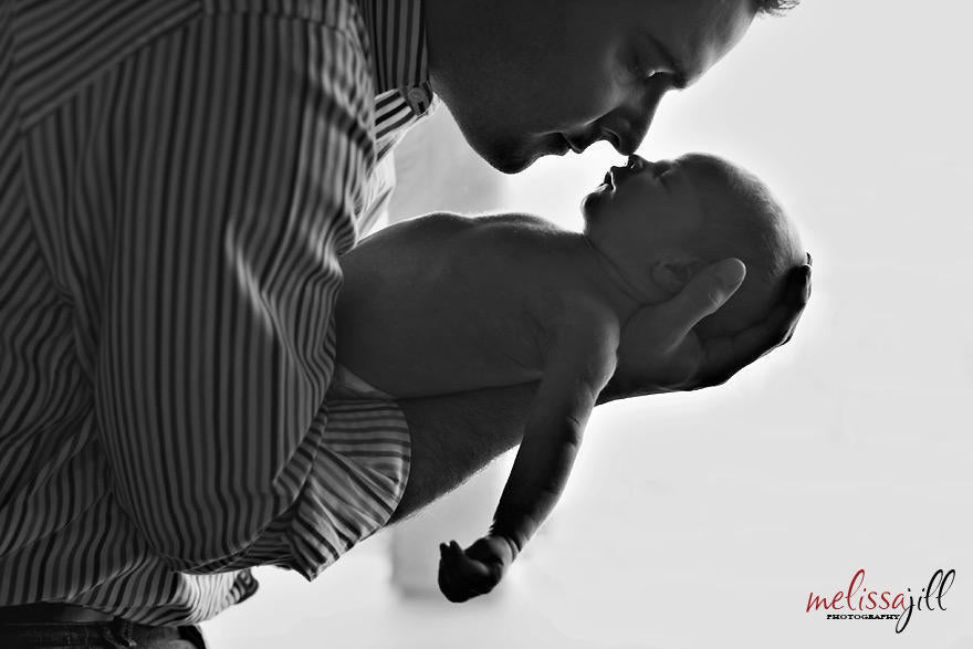 A black and white image of the side a father holding his newborn baby in his arms.