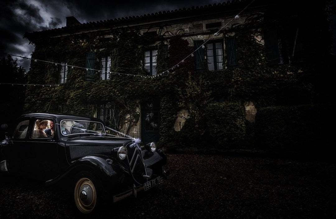 Bride and groom siting inside a black car parked in front of a house 