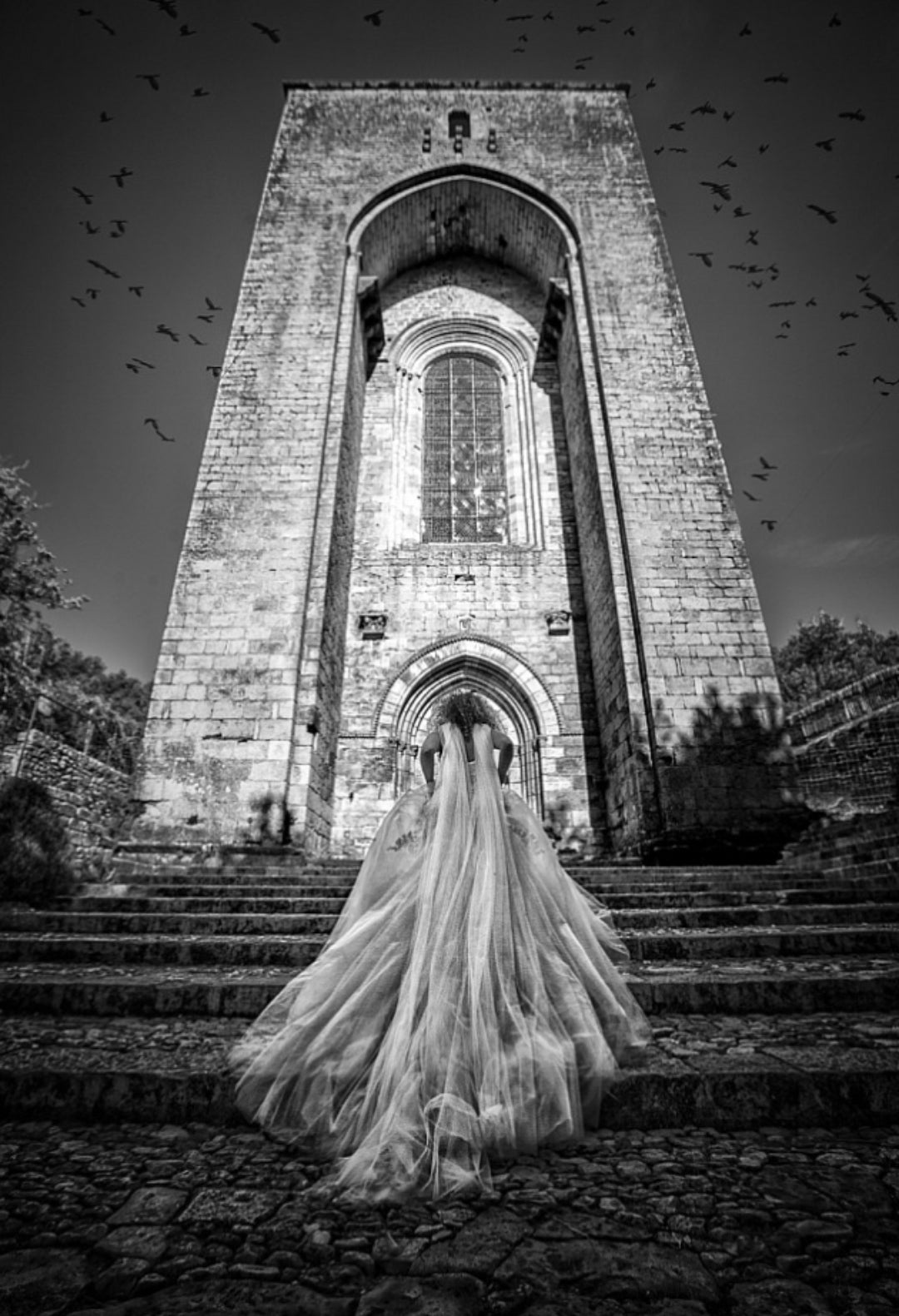 Black and white photograph of a bride climbing the stairs with the veil and the train of her dress following 