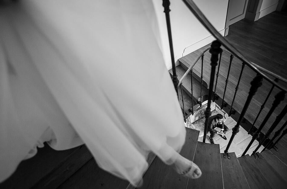 black and white image of a bride walking down stairs to groom