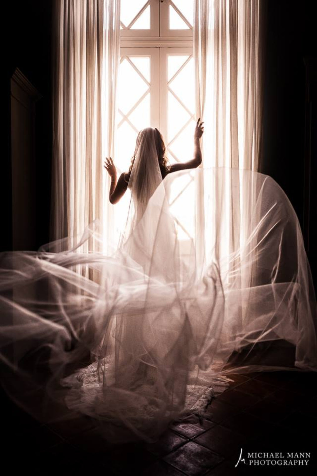 Dramatic back shot of the veil and train of the dress as the bride looks the other side through the window