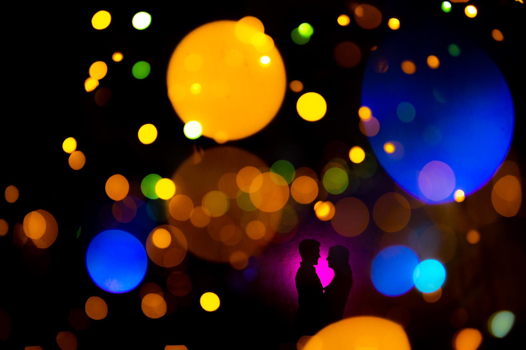 brightly colored lights in the image with silhouette of two people facing each other