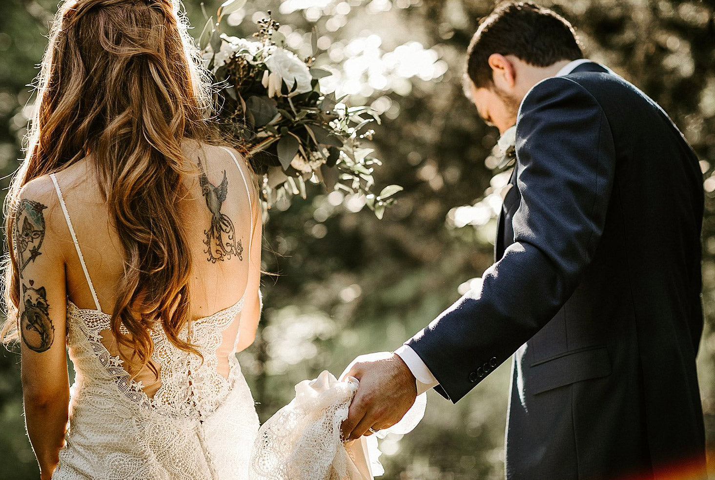 a wedding couple walking in while the groom is holding up the bridal dress