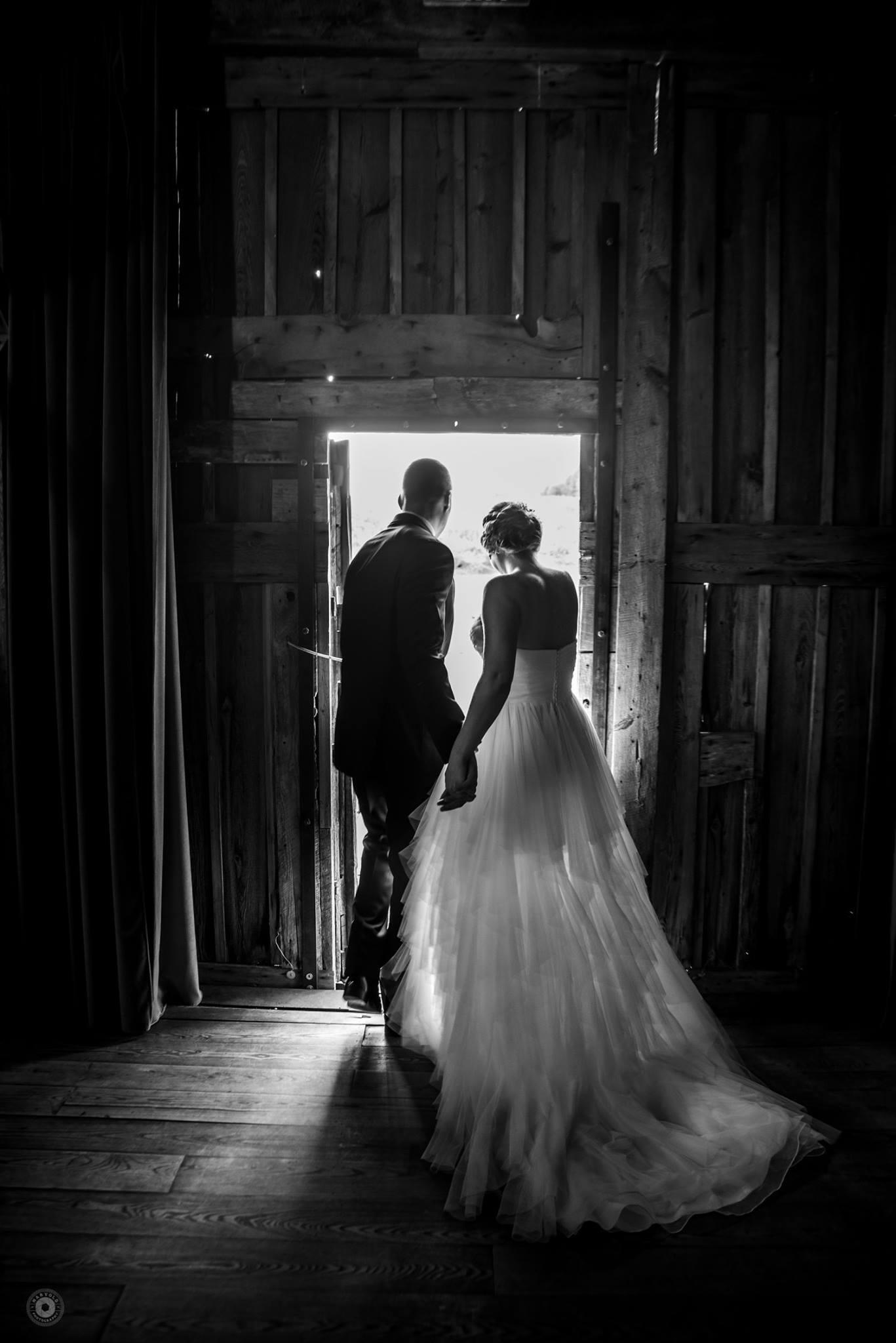 couple walking through doorway of a barn from dark inside to light outside