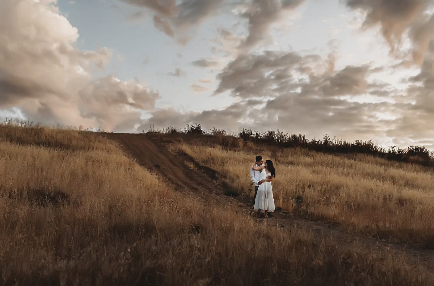 a couple standing and posing on a trail amidst grassy land