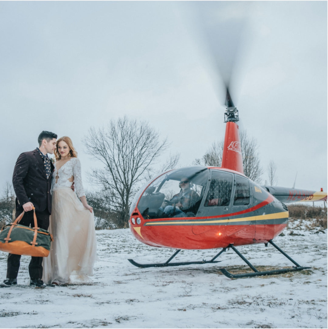 A bride and groom posing in front of a helicopter 