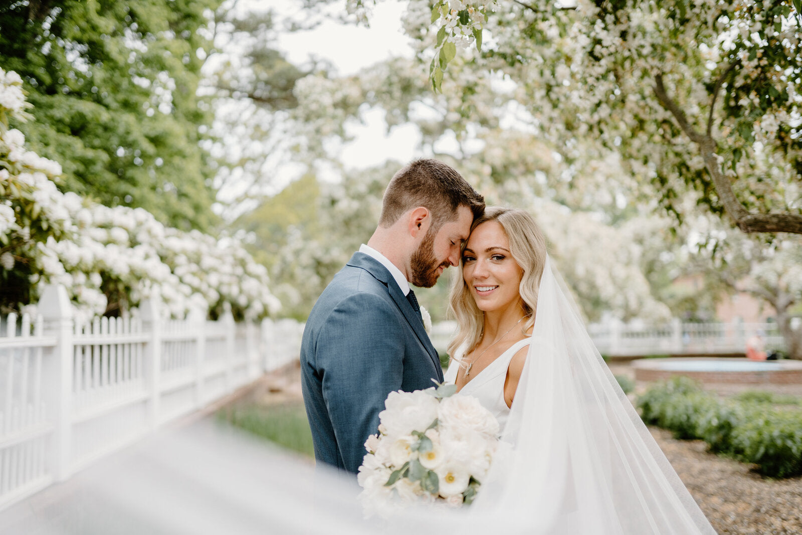 a wedding couple touching their heads together and posing while the bridal veil flows towards the camera