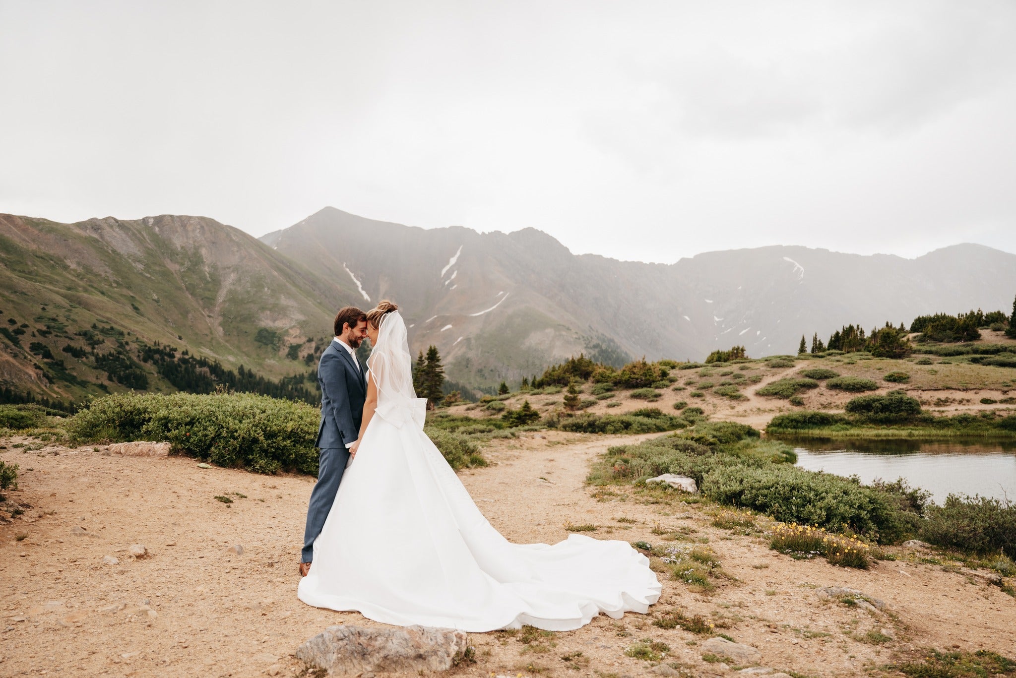 a wedding couple standing on a hilly dirt road in their wedding attire