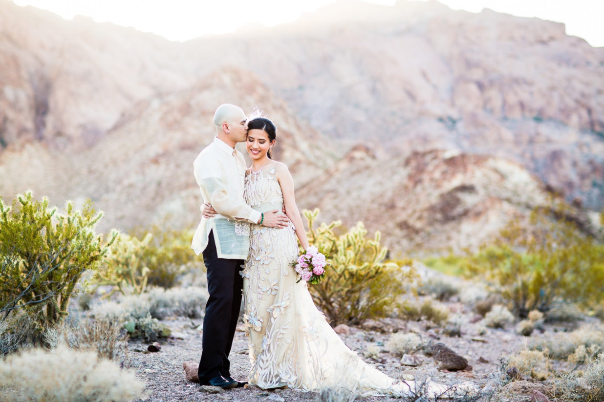 A couple posing in the outdoors with the groom kissing the bride on the forehead