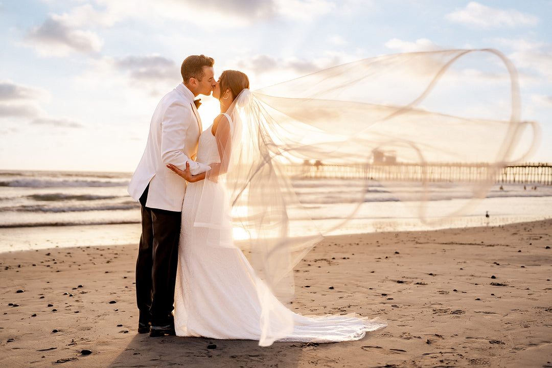 a couple kissing on the beach while the bridal veil is blowing in the wind