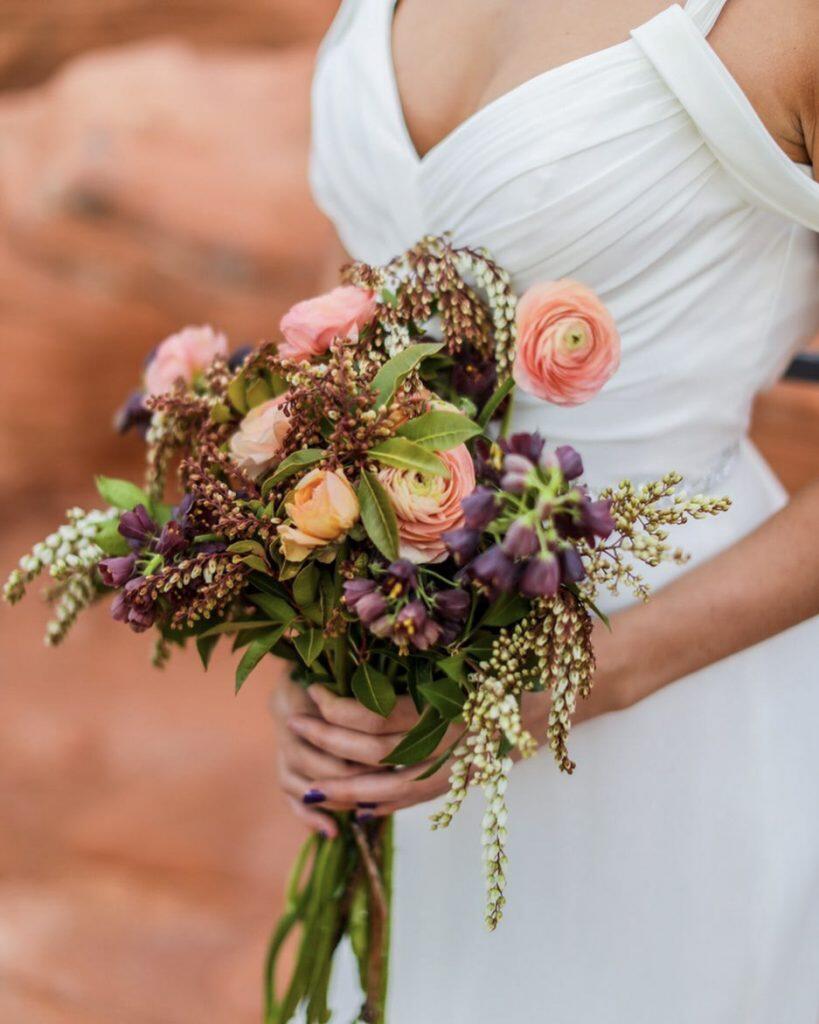 a close up shot of a bride standing while holding a bouquet in her hands