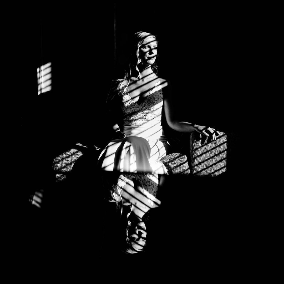 A monochrome portrait of a bride sitting on a coach as her reflection form on the table placed ahead