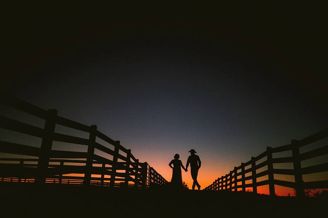 Silhouette of a couple posing for a photograph in a pathway bordered by fences 