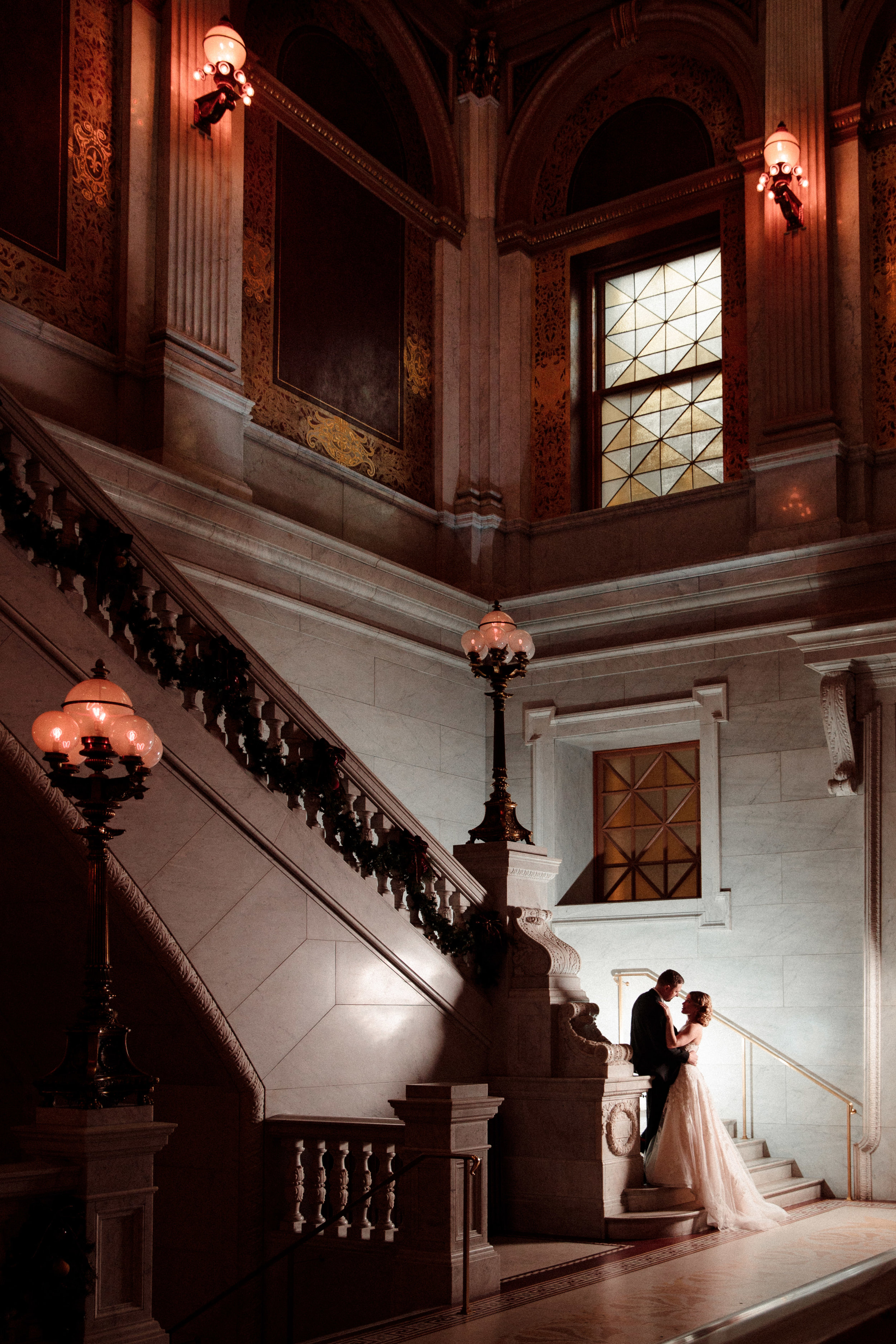 A bride and groom posing at the edge of a stairway while looking into each other's eyes