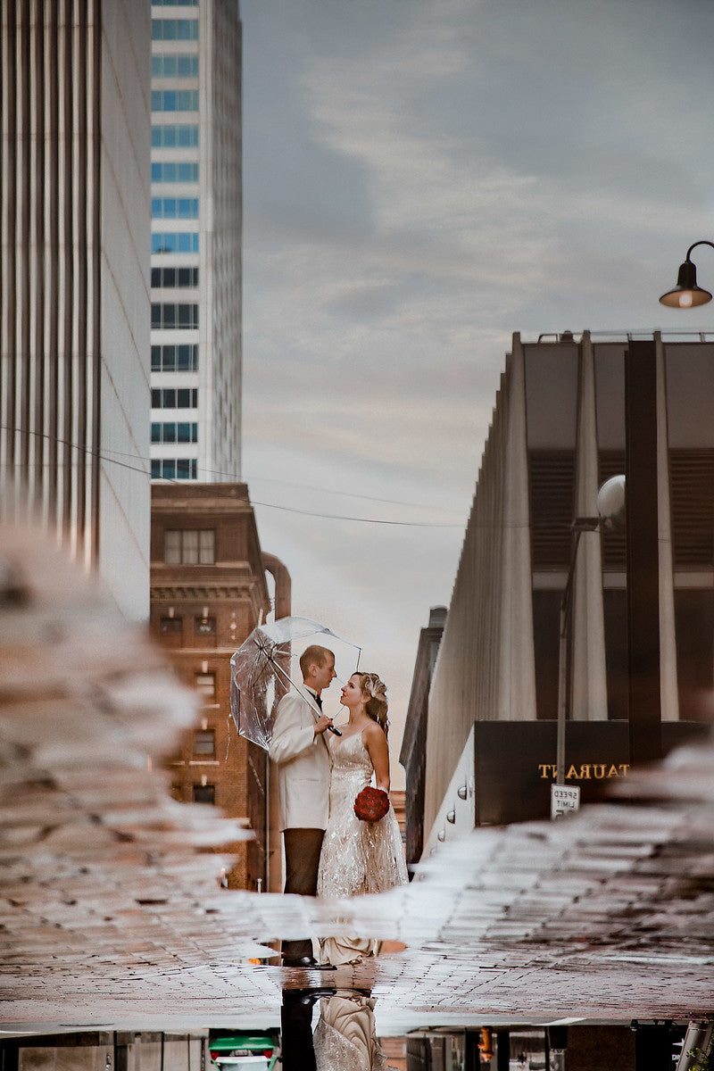 Gorgeous capture of a bride and groom posing under an umbrella through a reflection on the water on the floor