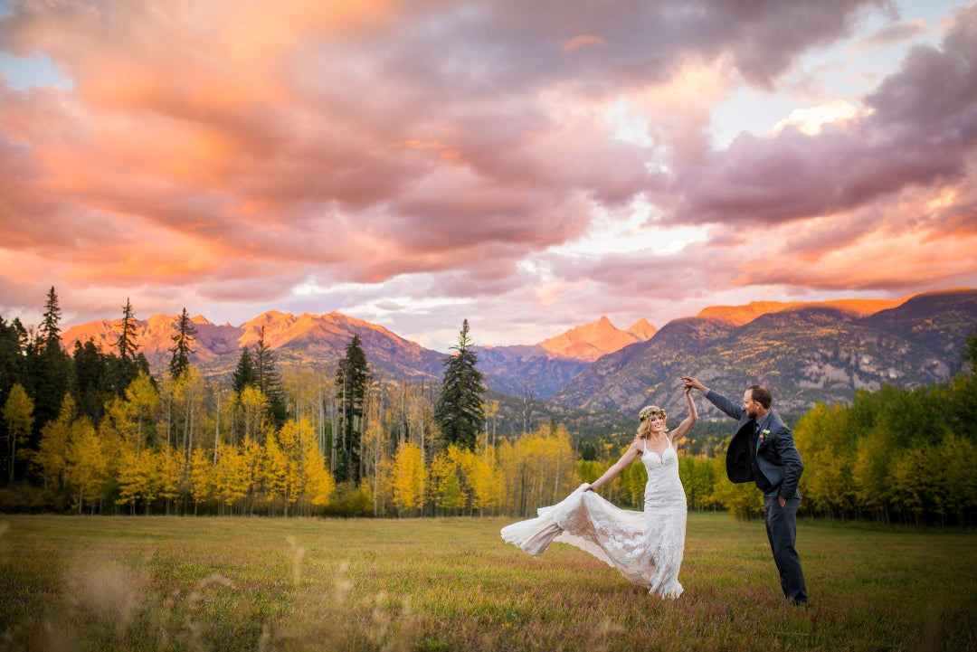 Bride swirling while holding the train of her dress from one hand and the groom's hand from the other in a natural setting