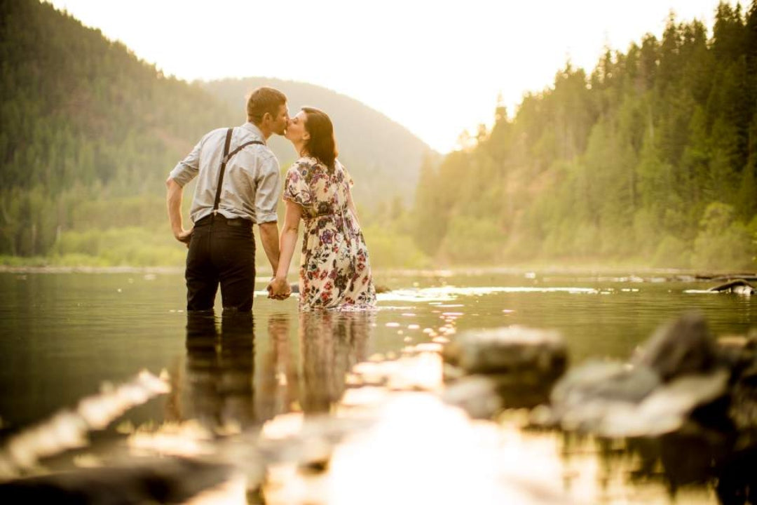 A couple kissing and holding hands while standing knee deep in lake water