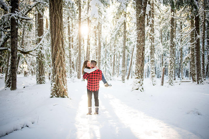 man carrying woman in a snow covered forest at sunset