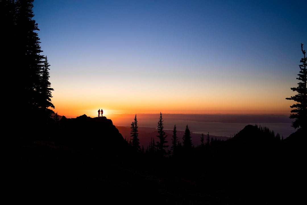 Silhouette of a couple standing on top of a cliff as the sun sets behind them