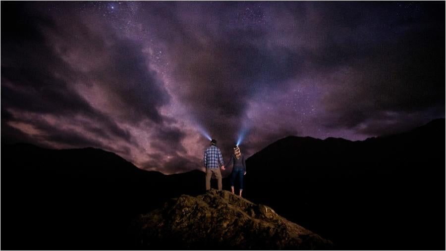 dark and starry night photo showing stars, clouds and a couple holding hands wearing headlamps