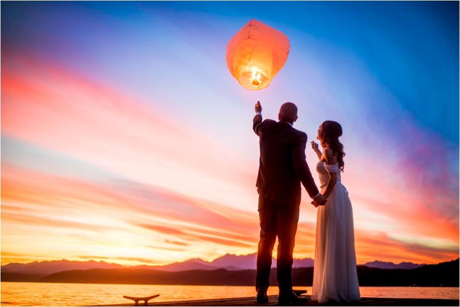 couple letting a lit lantern float off into the sky near a lake at sunset