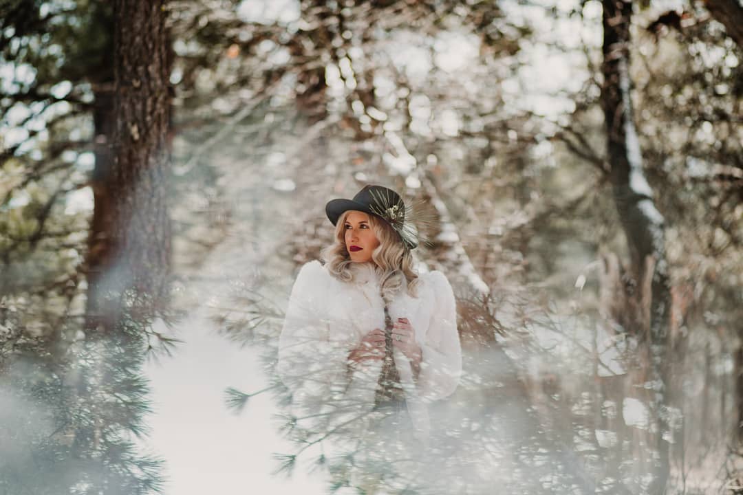 A bride wearing a stylish fedora looking leftward as the reflections of the window blend around her