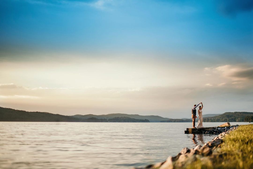 a groom twirling the bride holding her hand beside a lake