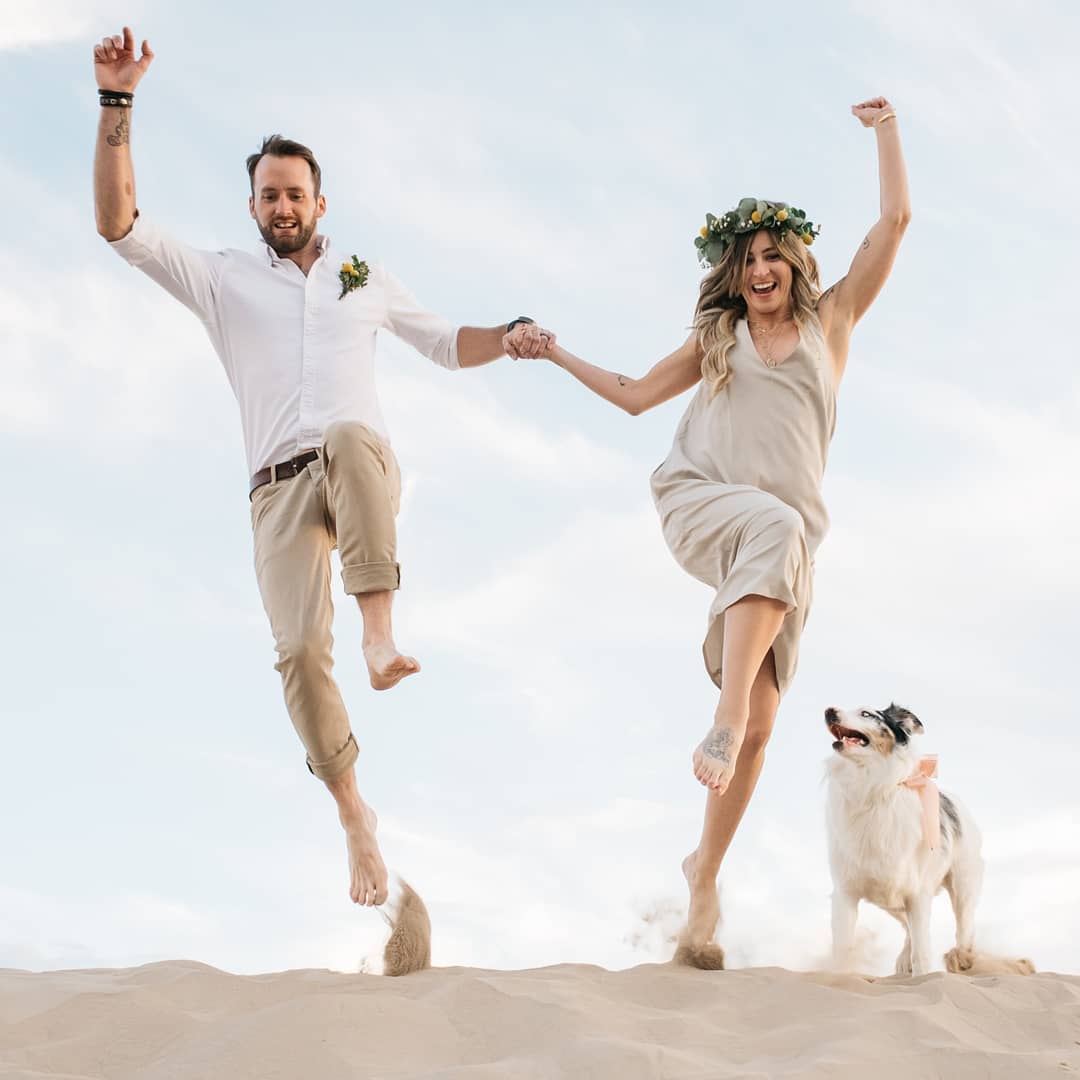 Low-angle shot of a bride and groom jumping with a dog at the side