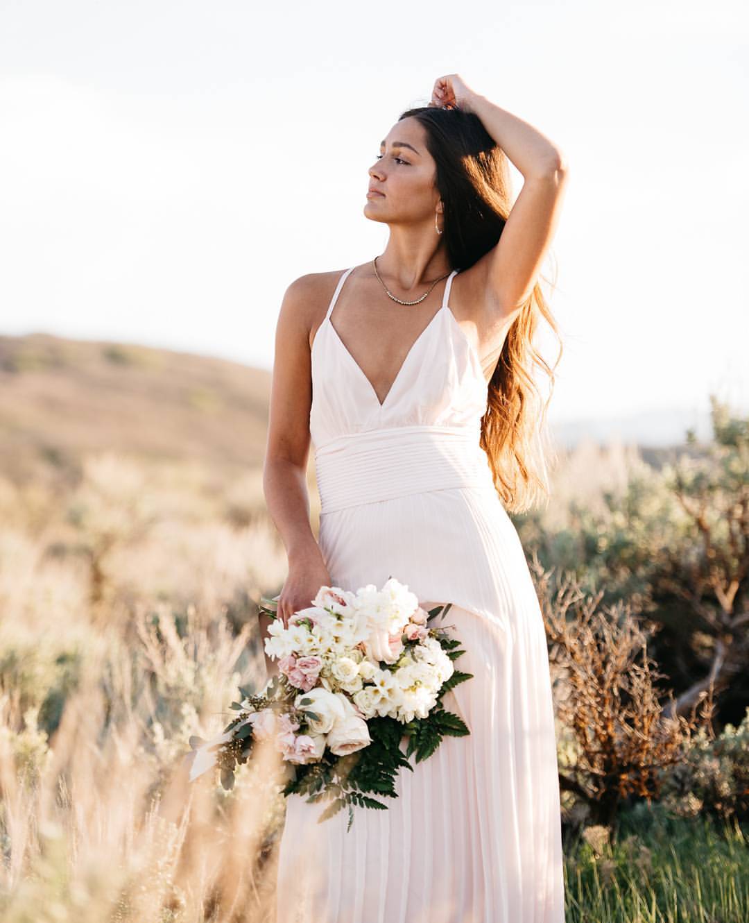 A bride posing with a bouquet out in a farm