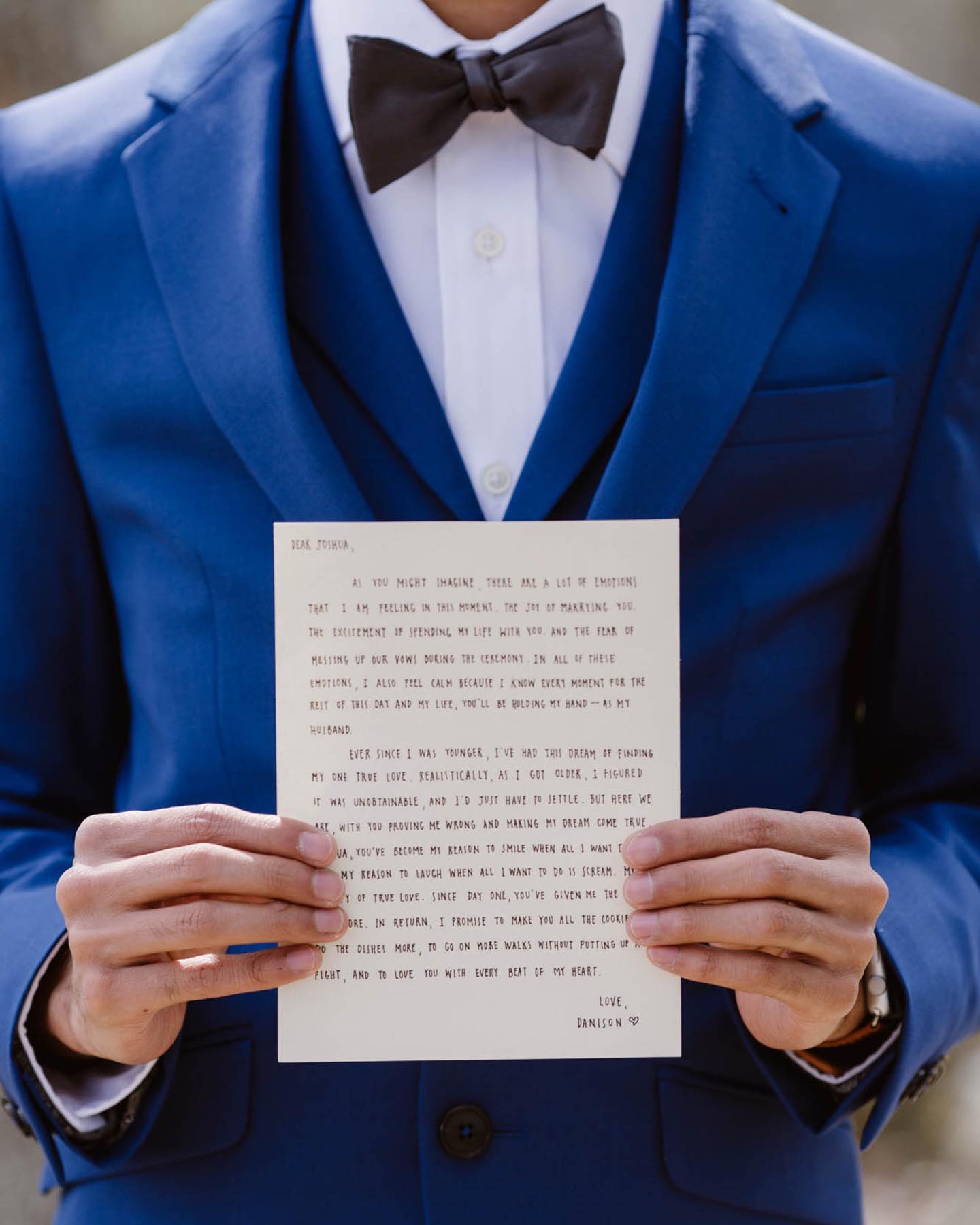 a groom in his wedding attire holding a love letter facing it towards the camera