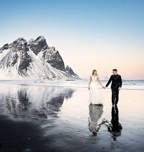 a wedding couple on the beach in front of a snowcapped hill 