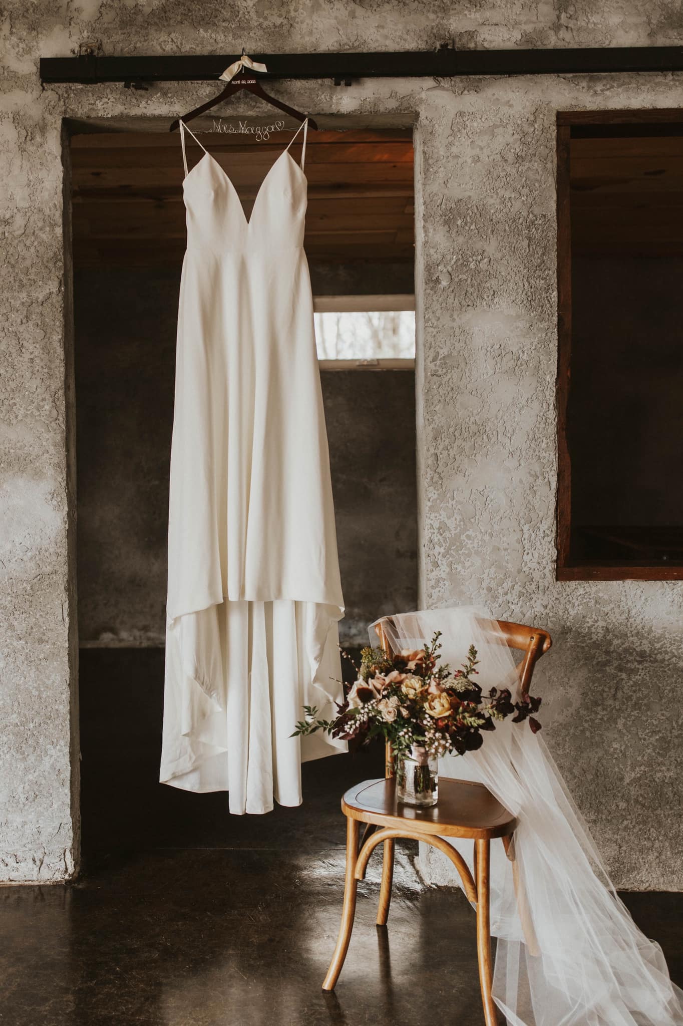 a bridal dress is hanging while the wedding veil and bouquet are kept beside