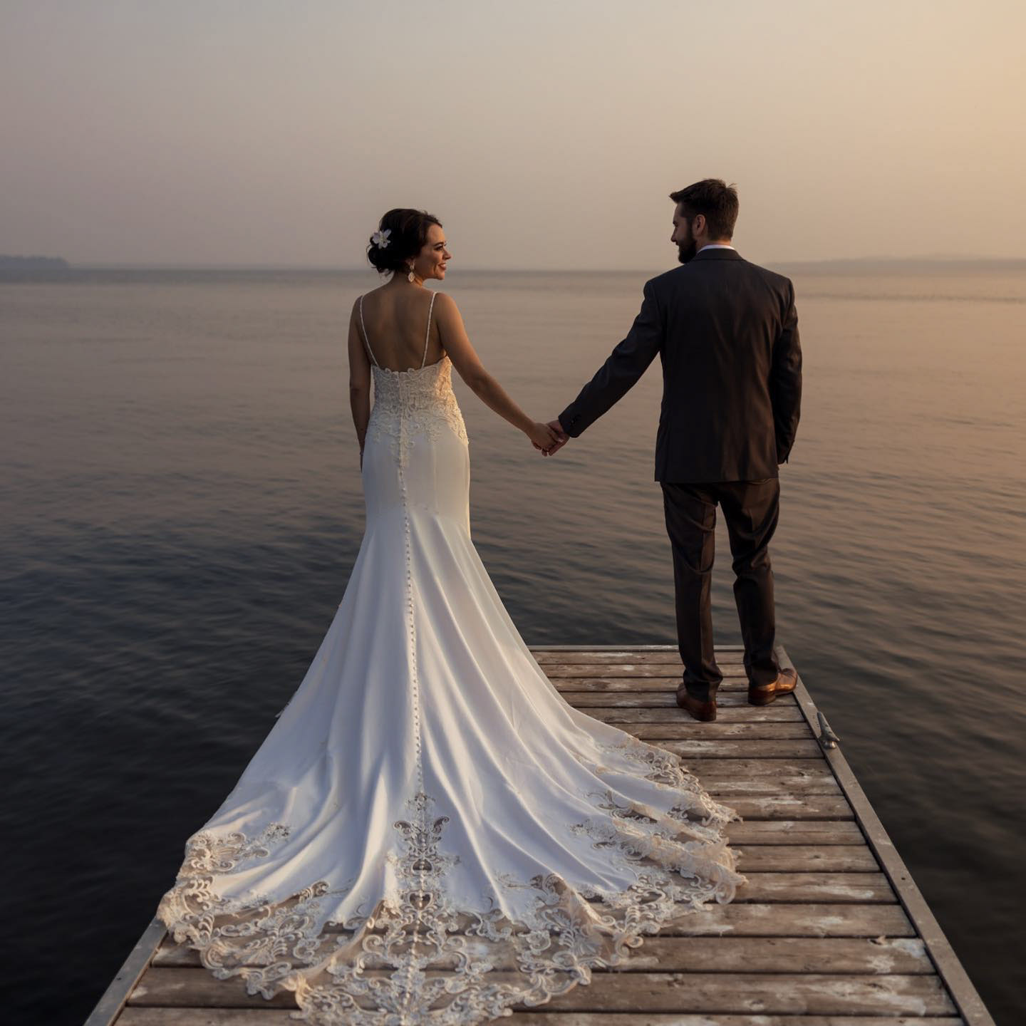 a wedding couple holding hands on a small pier 