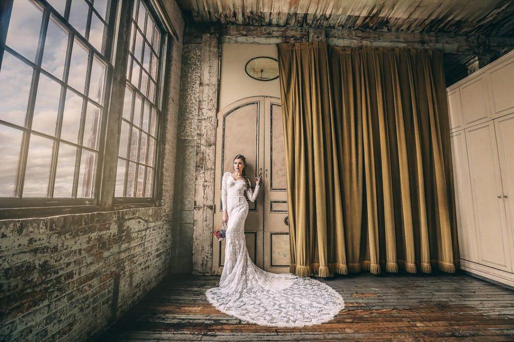 a bride in her wedding attire posing in a very old looking room with large windows