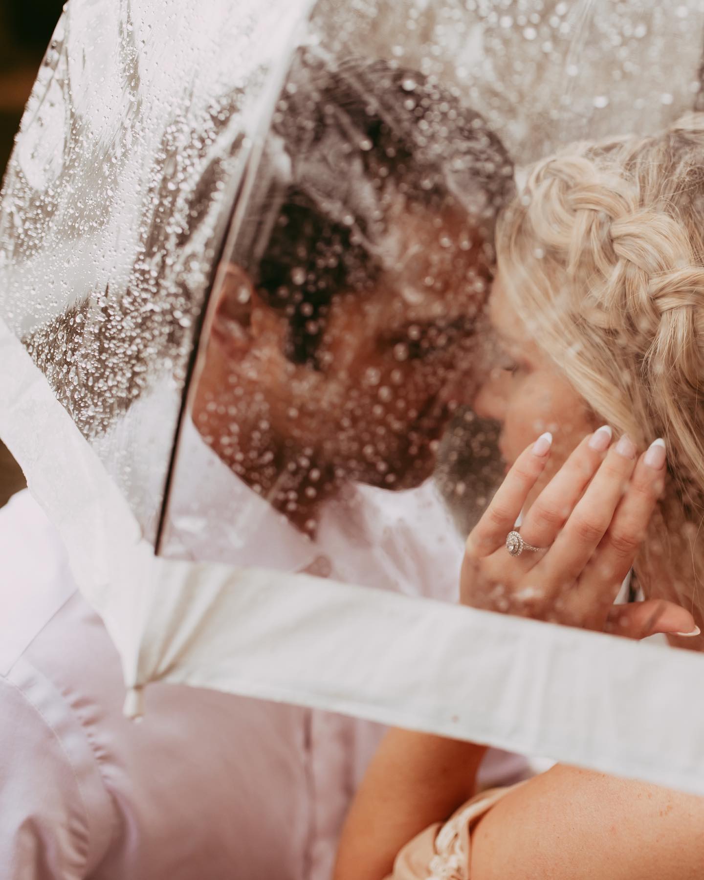 a wedding couple sharing a close moment under a transparent umbrella with rain drops on it