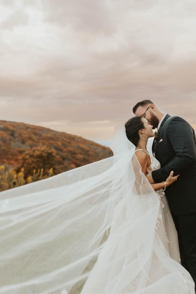 a newly wed couple sharing an intimate moment in their wedding attire with a cliff behind them