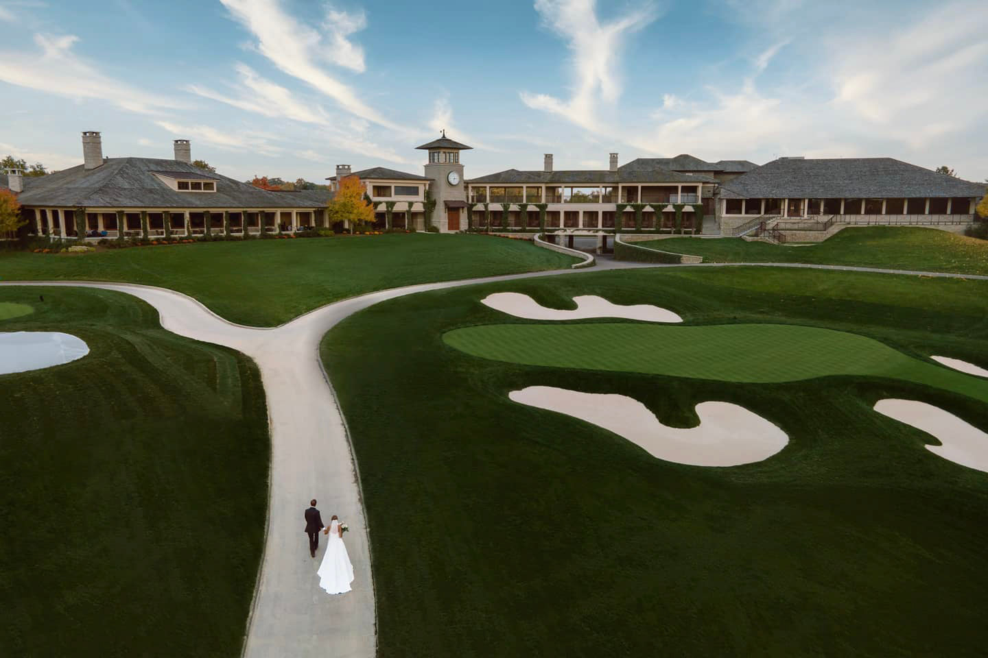 a drone view of a couple in their wedding attire walking through a golf course