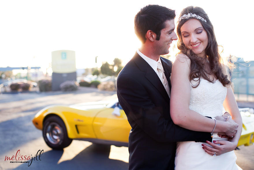 An outdoor wedding photography image of the bride and groom in an embrace, with the groom's yellow Corvette in the background behind them.