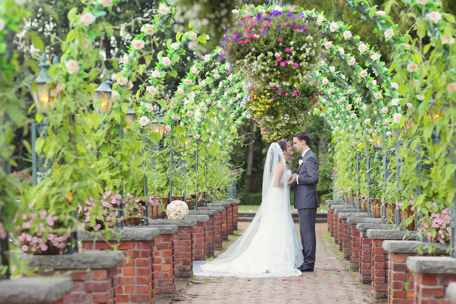 A wedding image of the couple standing face to face under an arch of flowers.