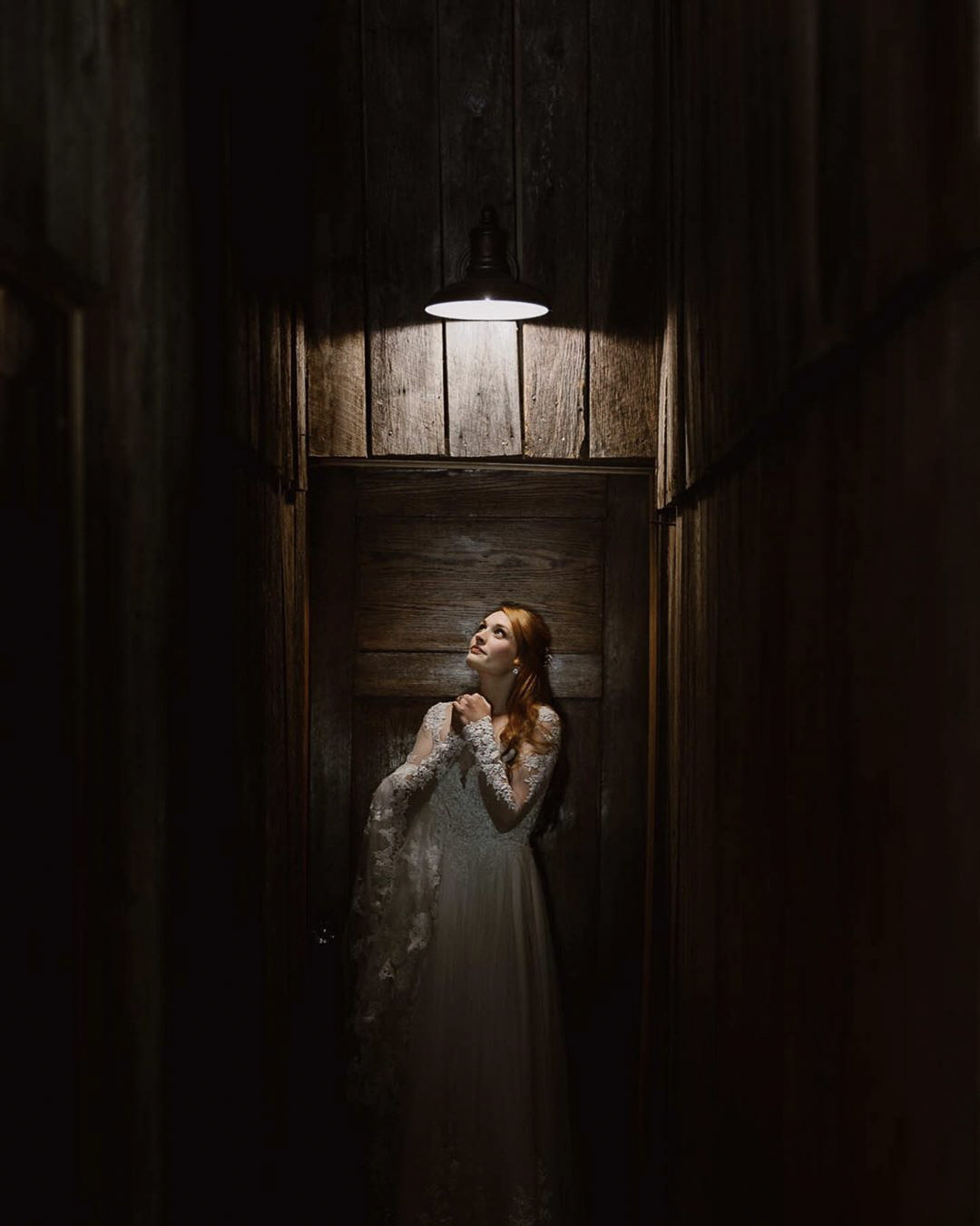 a bride looking up in a dimly lit room with only one light shining on her from the top