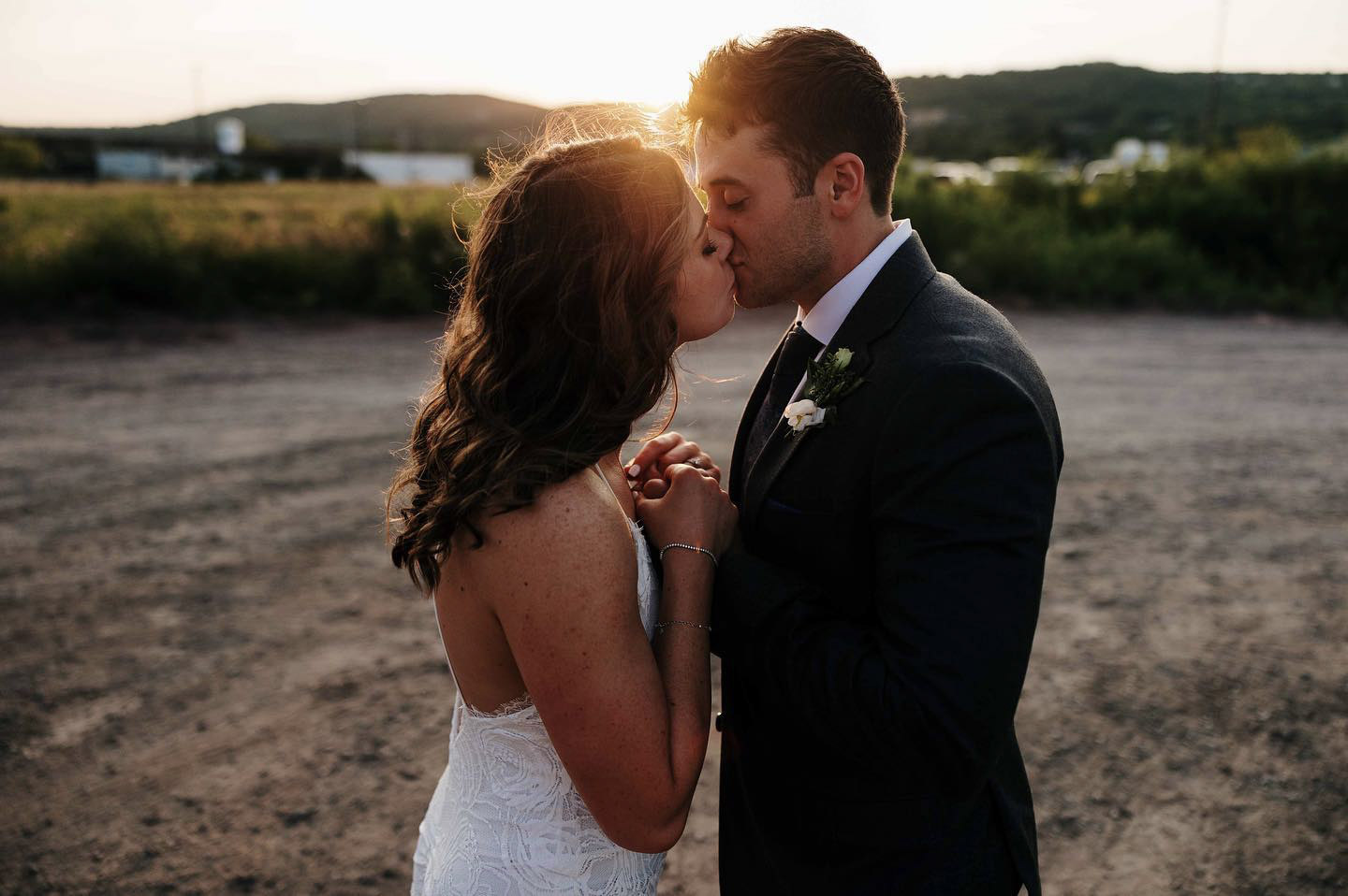 a newlywed bride and groom kissing while the sun sets behind them