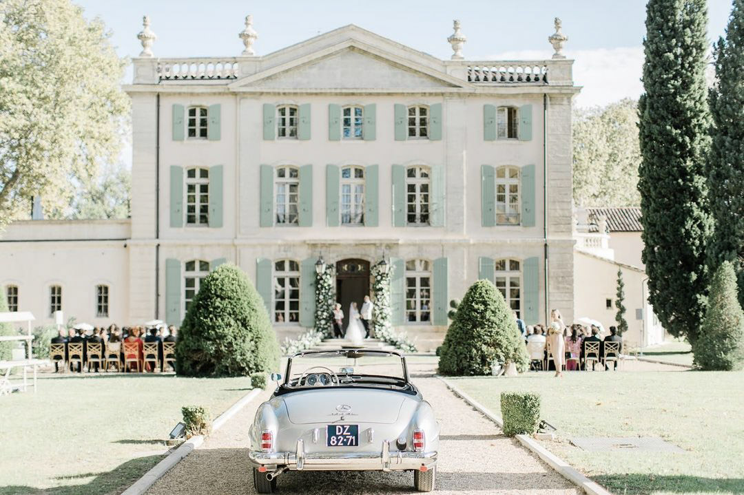 a wedding ceremony infront of a grand building with a car in the front