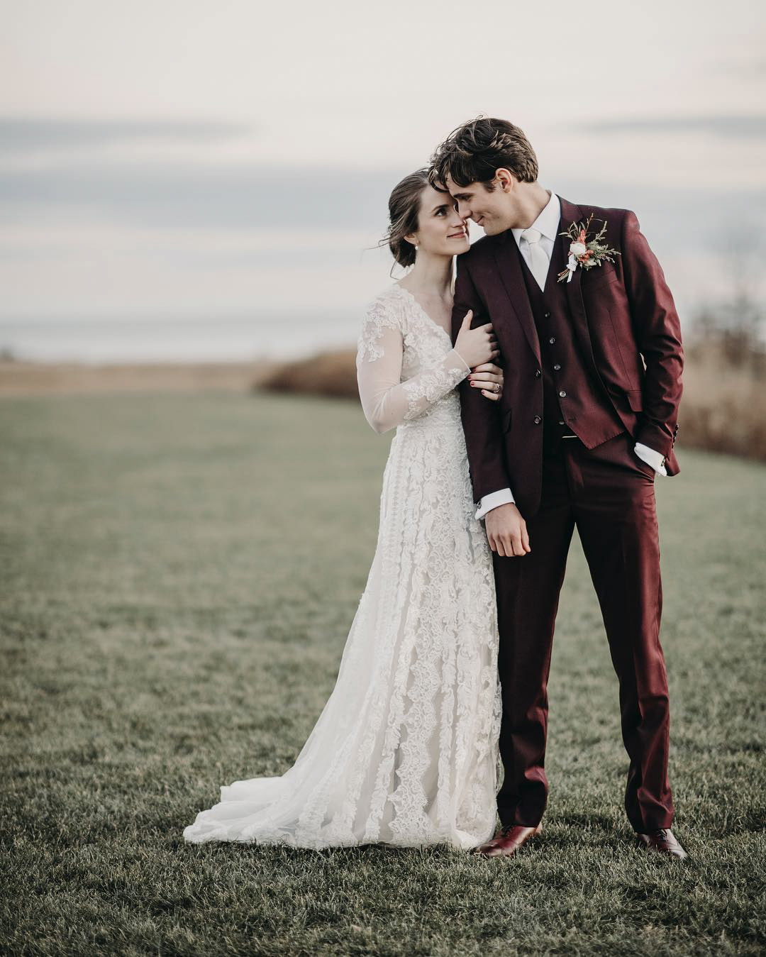 a bride and groom standing while the bride is holding the groom's hand 