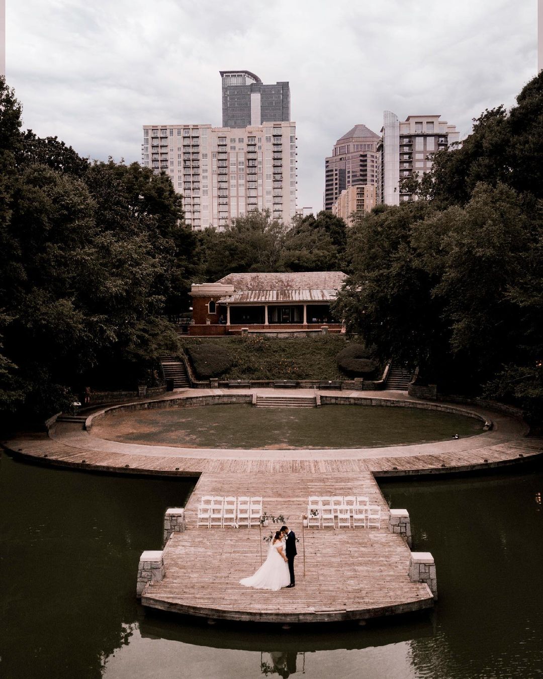 a aerial shot of a couple kissing in their wedding attire while some buildings are visible behind them