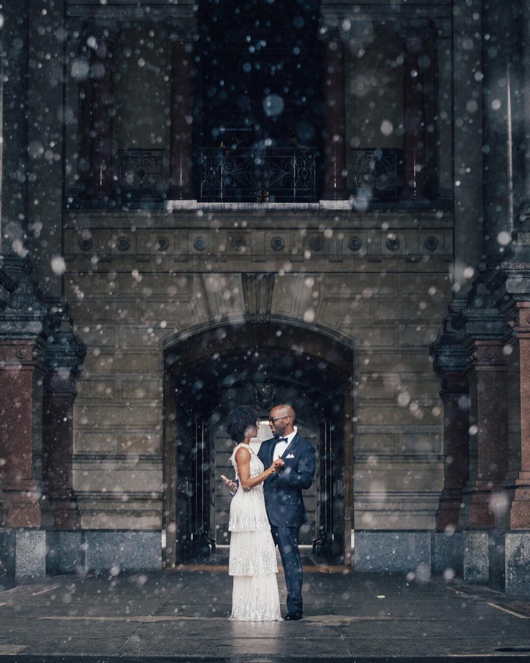 A bride and groom posing in front of a doorway during snowfall