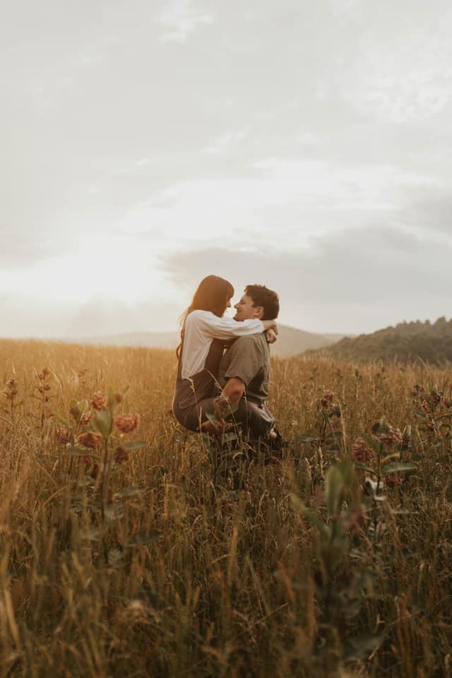 a couple posing in a hayfield where the groom has lifted the bride in his arms